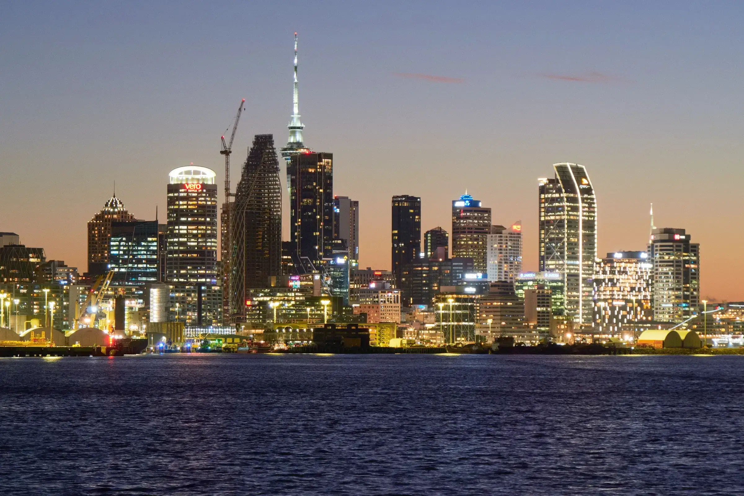 The Auckland city skyline and Sky Tower lit up at dusk across the harbour